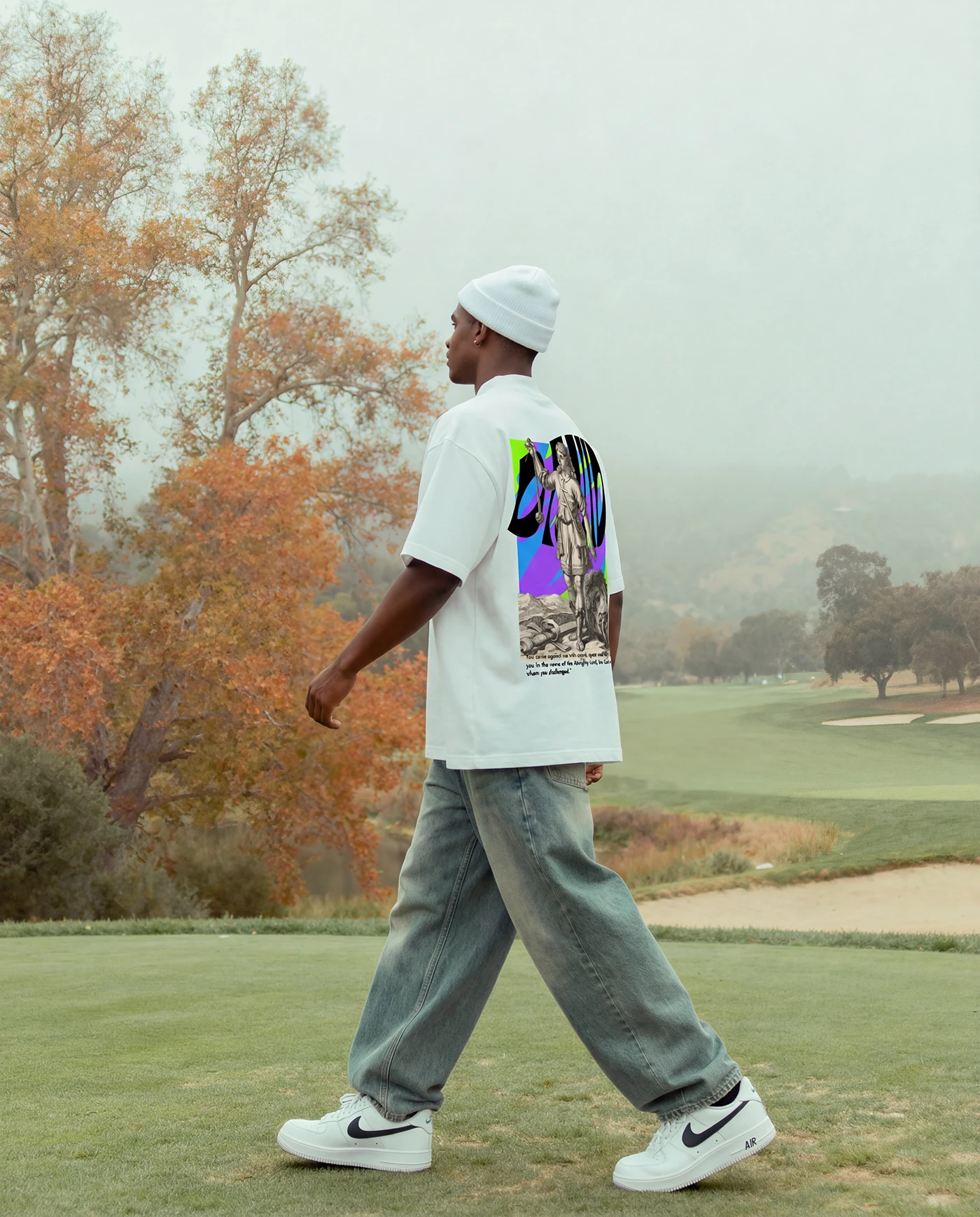 Model walking across a golf course in the Timeless tee and a white beanie